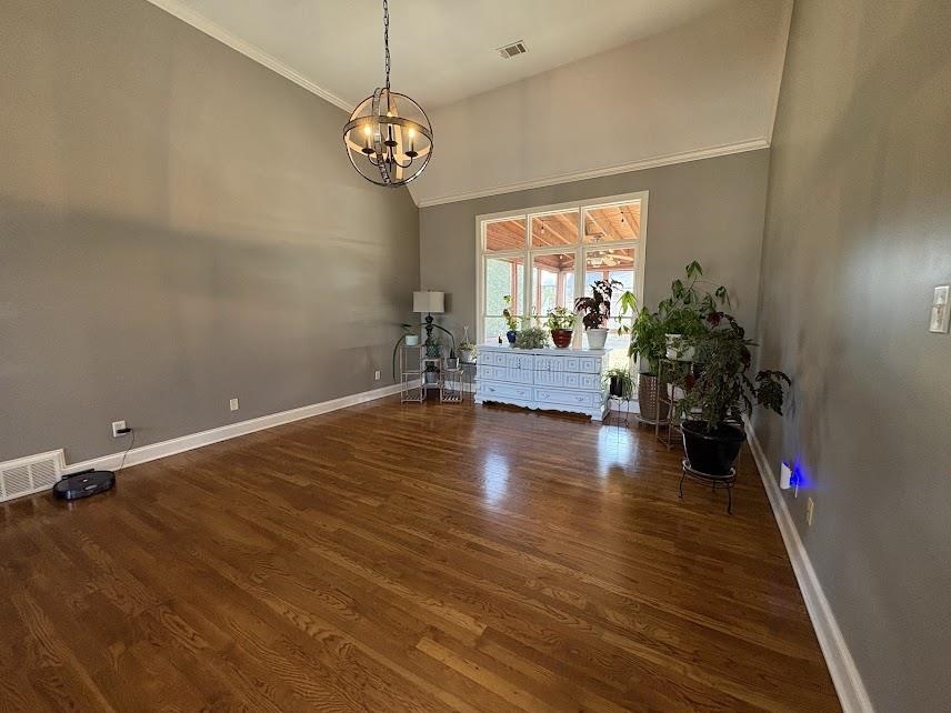 Dining area with a high ceiling, dark wood-style floors, a chandelier, and crown molding