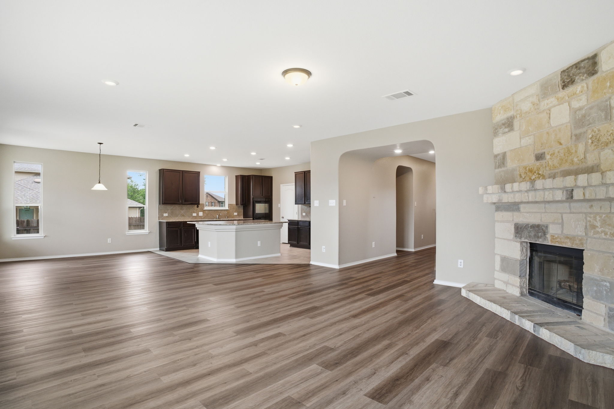 670 Landon Samuel Loop Pflugerville, TX 78660 - Photo 3 of 22 Spacious interior featuring wood-finish flooring, a stone-faced fireplace with hearth, recessed lighting, and an open-concept kitchen with dark wood cabinetry and a central island