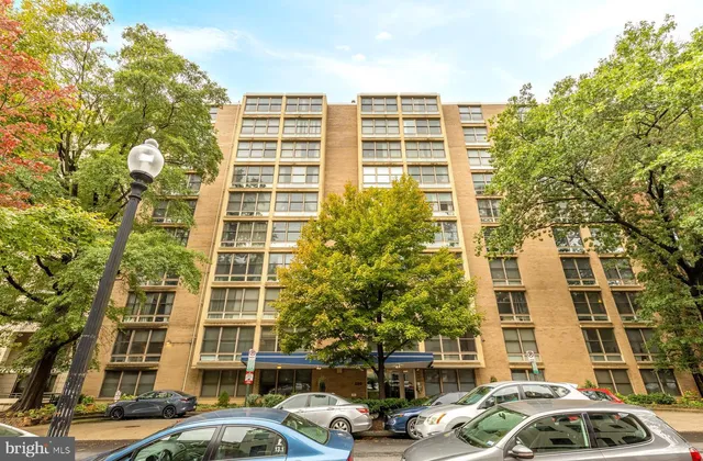 a front view of a building with lot of cars and trees