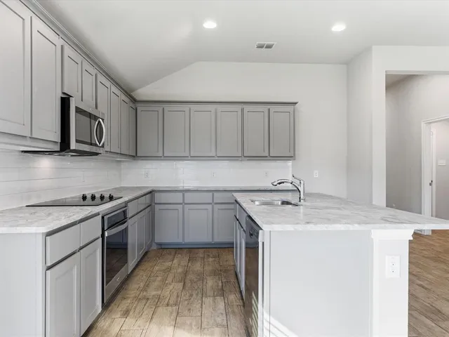 a large kitchen with stainless steel appliances granite countertop a stove a sink dishwasher and a refrigerator with wooden floor