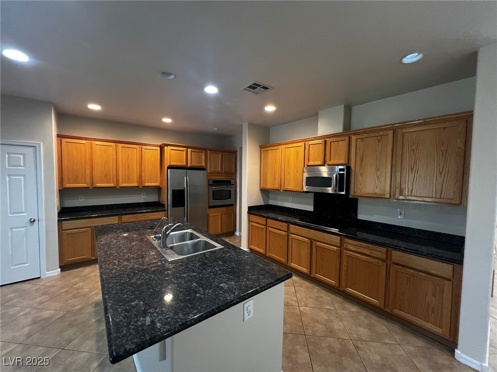 3417 West Birdwatcher Avenue North Las Vegas, NV 89084 - Photo 8 of 28 Kitchen featuring recessed lighting, stainless steel appliances, brown cabinetry, a center island with sink, and light tile patterned floors
