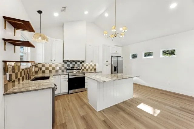 a large white kitchen with kitchen island a sink dishwasher a stove and a dining table with wooden floor