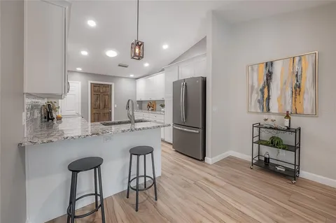 a kitchen with granite countertop a refrigerator a sink and white cabinets