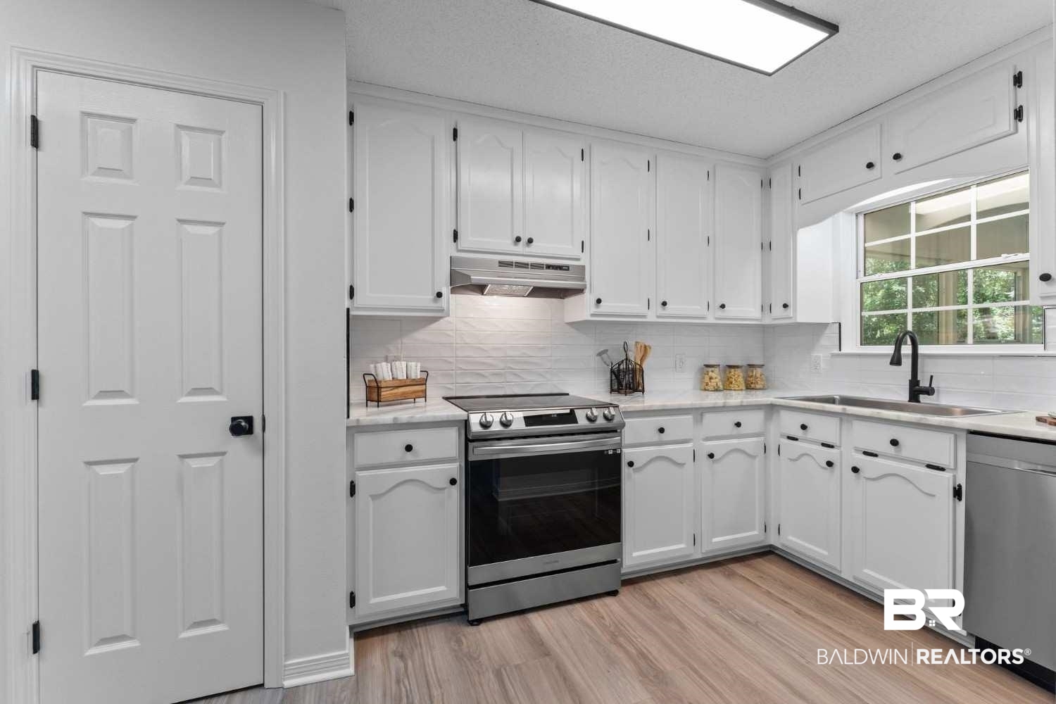 10251 Windmill Road Fairhope, AL 36532 - Photo 23 of 44 Kitchen with stainless steel appliances, under cabinet range hood, white cabinets, light wood-style floors, and backsplash
