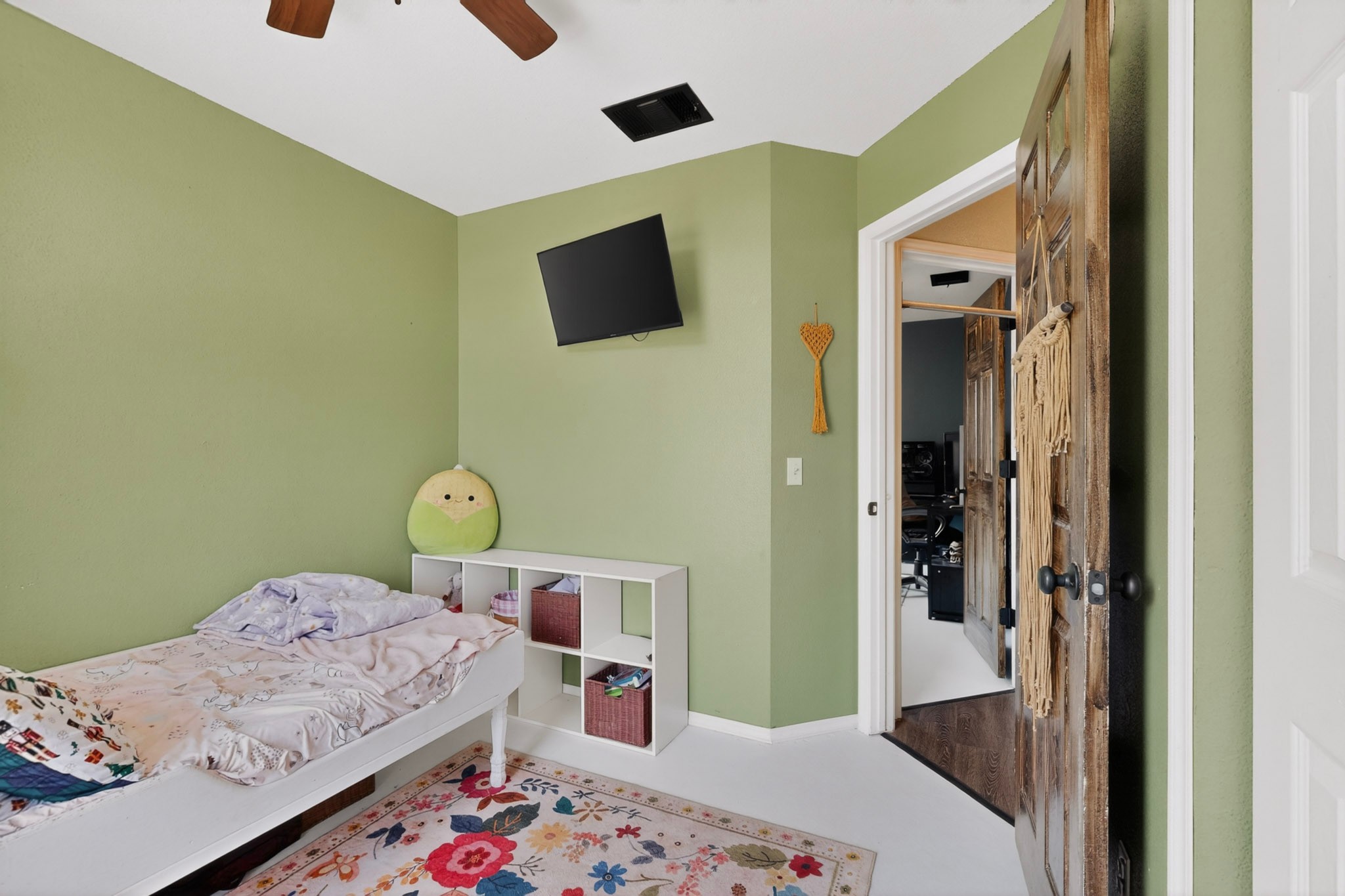 15104 Mimebark Way Austin, TX 78724 - Photo 25 of 38 Interior room featuring a wood-finish ceiling fan, wall-mounted television bracket, a white storage cube unit, and a solid wood paneled door with dark hardware
