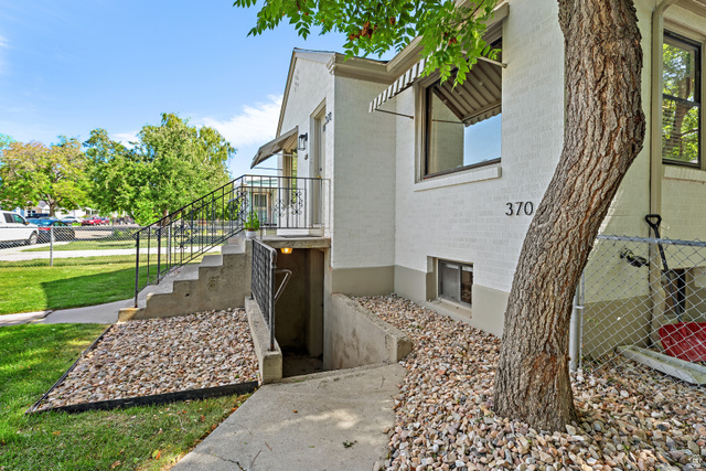 372 800 East Provo, UT 84606 - Photo 14 of 29 Exterior featuring a prominent mature tree, white brick facade, concrete steps with wrought iron railings, an entrance awning, and a lower-level access point