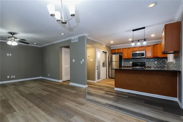 a view of an empty room and kitchen with wooden floor