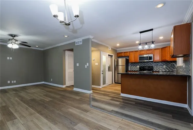 a view of an empty room and kitchen with wooden floor