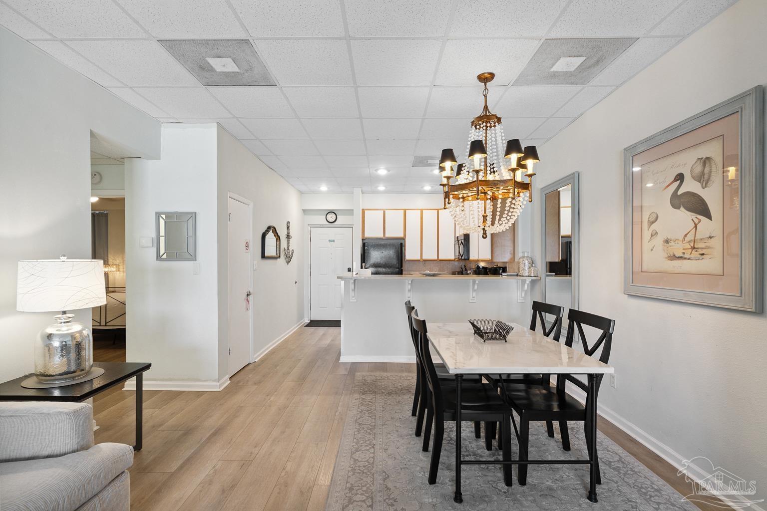999 Fort Pickens Road, Unit 204 Pensacola Beach, FL 32561 - Photo 12 of 48 a dining room with wooden floor a chandelier a wooden table and chairs