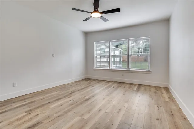 an empty room with wooden floor ceiling fan and windows