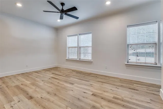 an empty room with wooden floor ceiling fan and windows