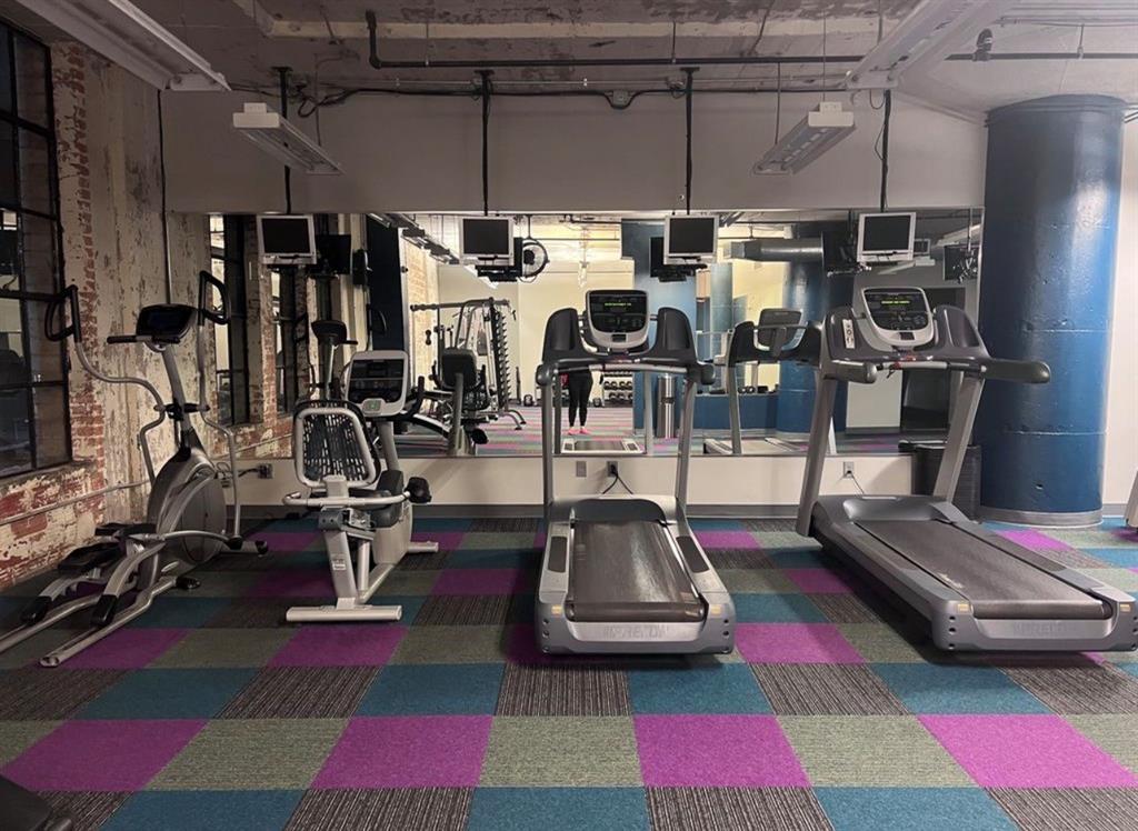 1122 Jackson Street, Unit 514 Dallas, TX 75202 - Photo 38 of 40 Fitness area featuring exposed brick walls, overhead lighting, a mirror wall, Treadmill, stair stepper