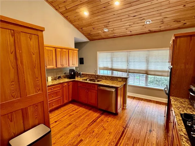 a kitchen with stainless steel appliances granite countertop wooden floors wooden cabinets a sink and a large window