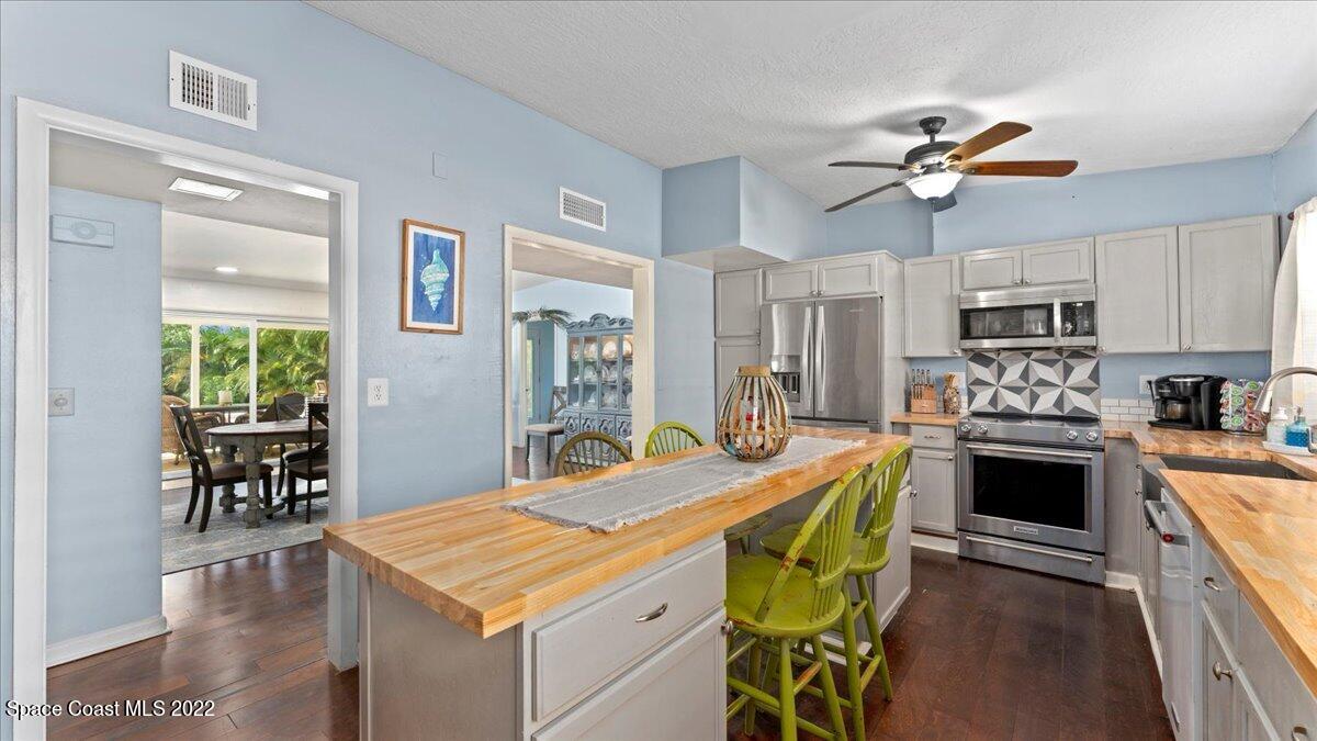 912 Bali Road Cocoa Beach, FL 32931 - Photo 3 of 48 a kitchen with stainless steel appliances kitchen island granite countertop a stove top oven a sink a dining table and chairs with wooden floor