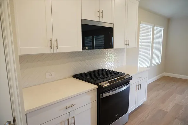 a kitchen with stainless steel appliances a stove top oven a sink a refrigerator white cabinets and wooden floor