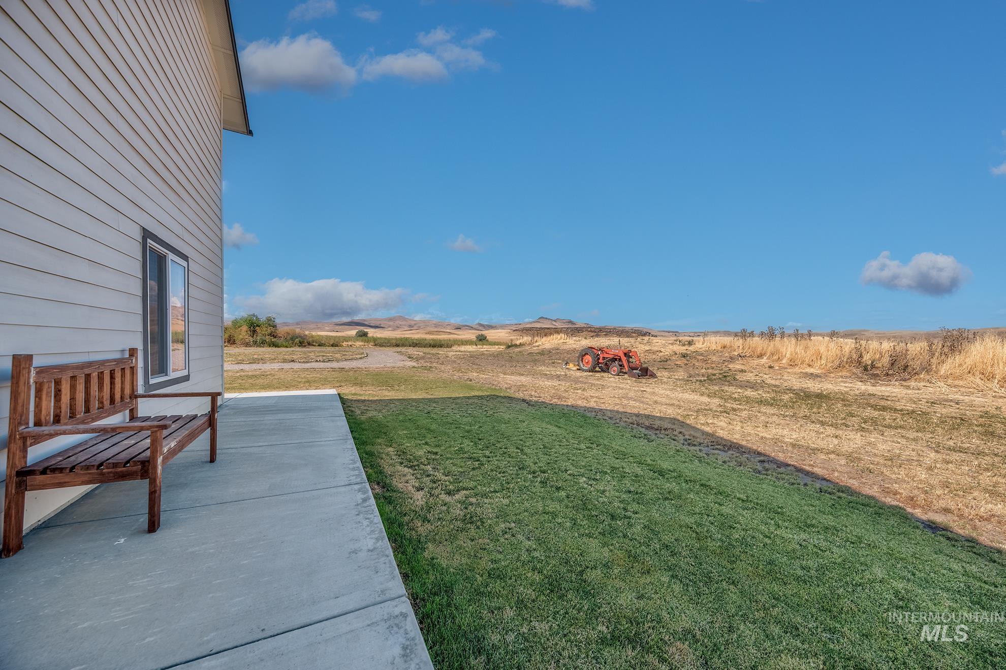 1049 Price Road Weiser, ID 83672 - Photo 34 of 47 Expansive side yard featuring a concrete patio, manicured lawn, and distant open fields with rolling hills