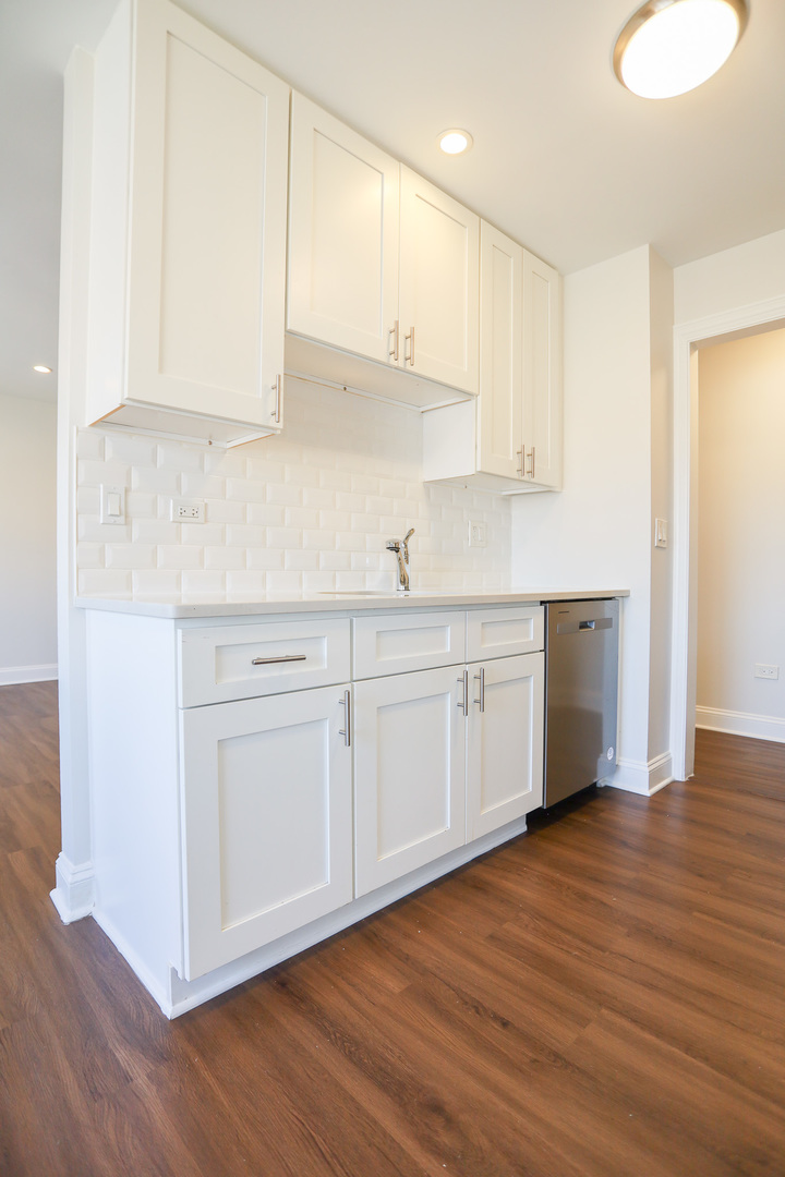 8651 West Foster Avenue, Unit 3A Chicago, IL 60656 - Photo 3 of 17 a kitchen with stainless steel appliances granite countertop a sink a stove and white cabinets with wooden floor