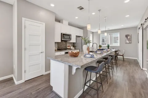 a kitchen with stainless steel appliances granite countertop a stove top oven a sink dishwasher a dining table and chairs with wooden floor