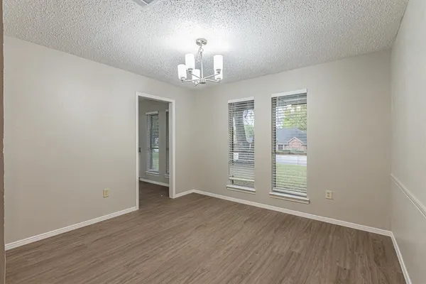 an empty room with wooden floor chandelier and windows