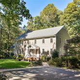 a view of a white house next to a yard with big trees