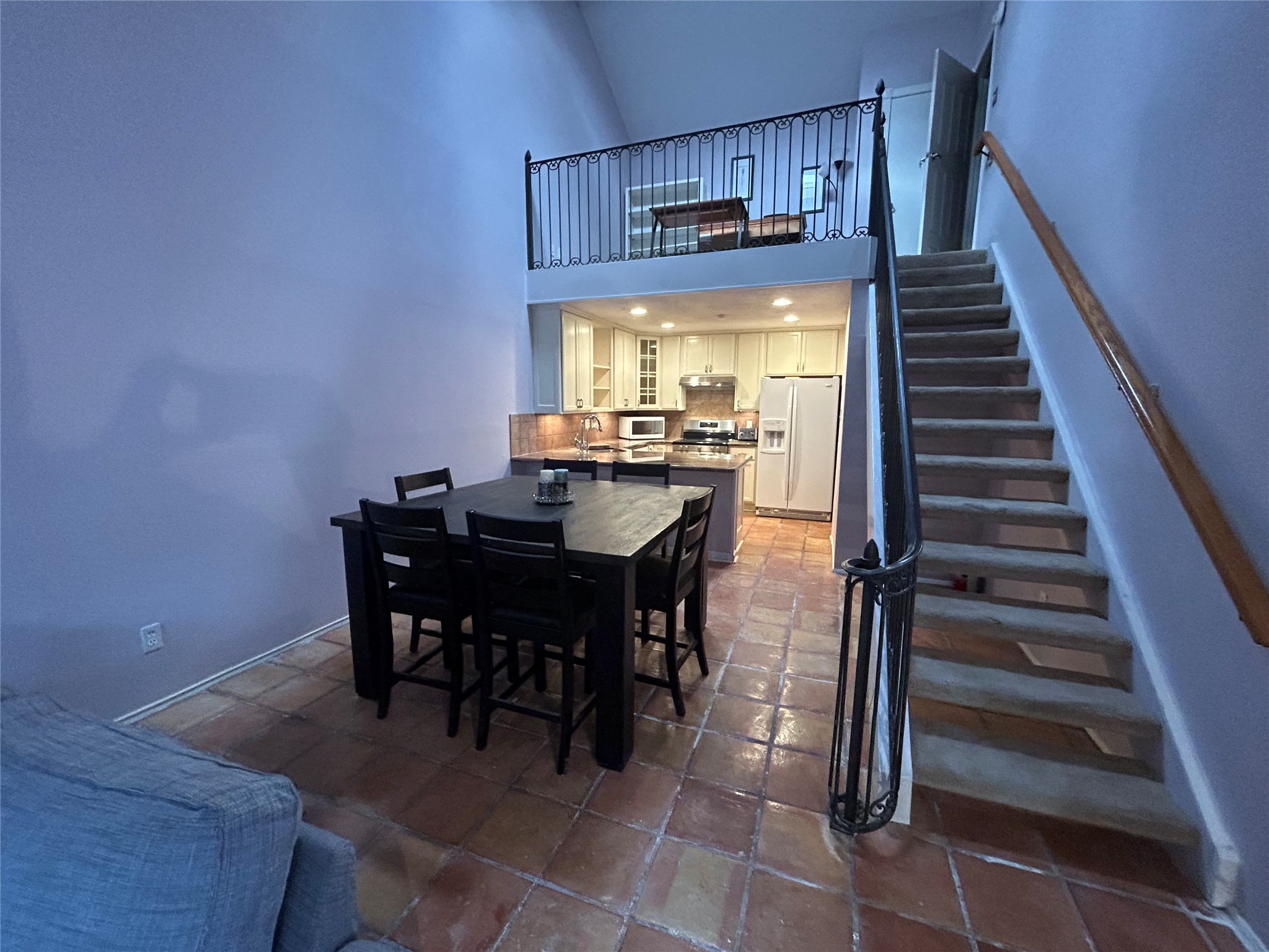 13034 Leader Street, Unit 965 Houston, TX 77072 - Photo 2 of 32 This photo showcases an open-concept living space with high ceilings and a loft area. The kitchen features modern appliances and is adjacent to a dining area with a large table. A staircase leads to the loft, adding charm and additional space. The room is well-lit and has a warm, inviting atmosphere.