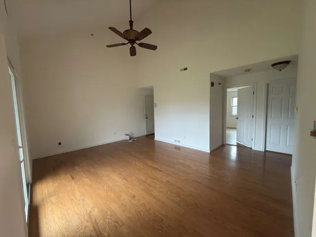 an empty room with wooden floor ceiling fan and windows