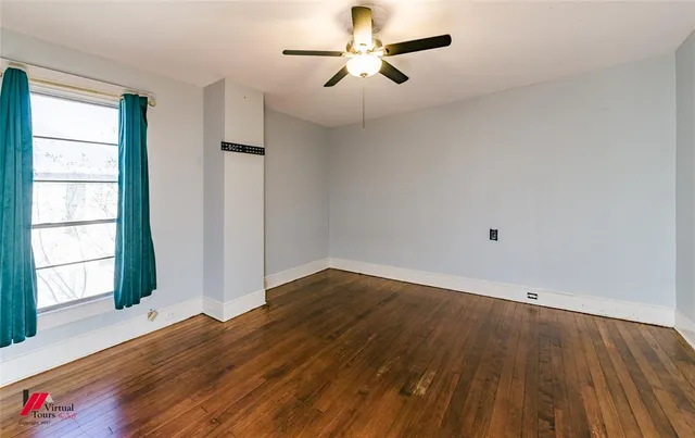 an empty room with wooden floor chandelier fan and windows