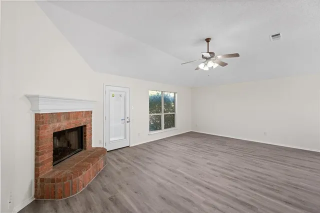 a view of an empty room with wooden floor fireplace and a window
