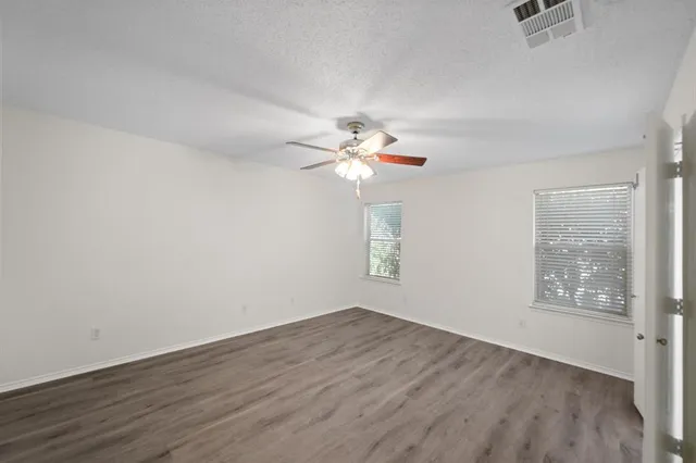 an empty room with wooden floor fan and windows