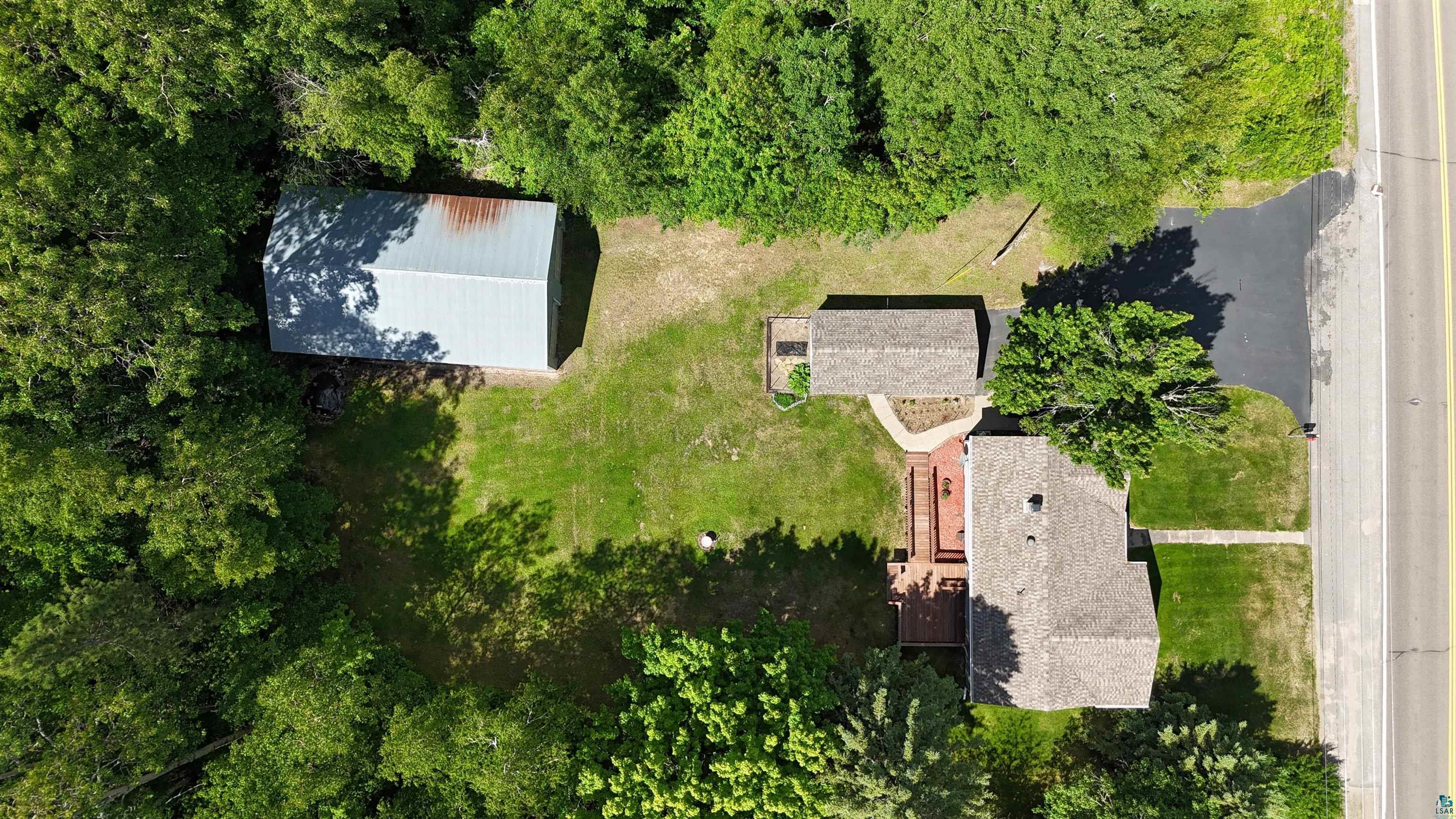 10614 Moose Lake Road Orr, MN 55771 - Photo 9 of 44 Expansive property featuring a main residence with a shingle roof, a detached auxiliary building with a shingle roof, a separate metal-roofed outbuilding, a paved driveway, and a wooden deck structure