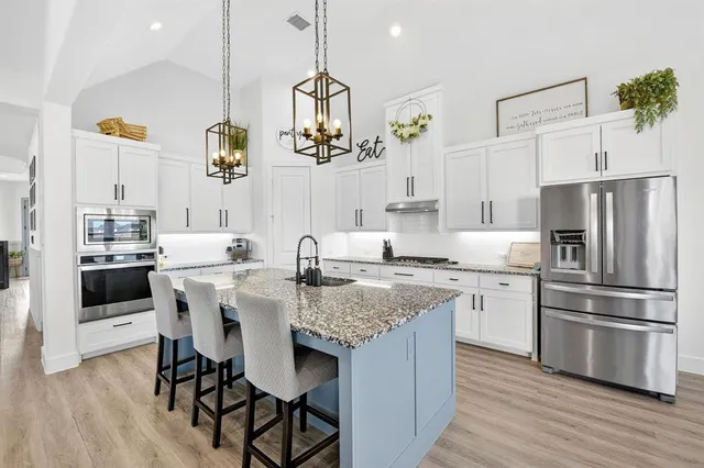 a kitchen with stainless steel appliances granite countertop a sink a stove a refrigerator and island with wooden floor