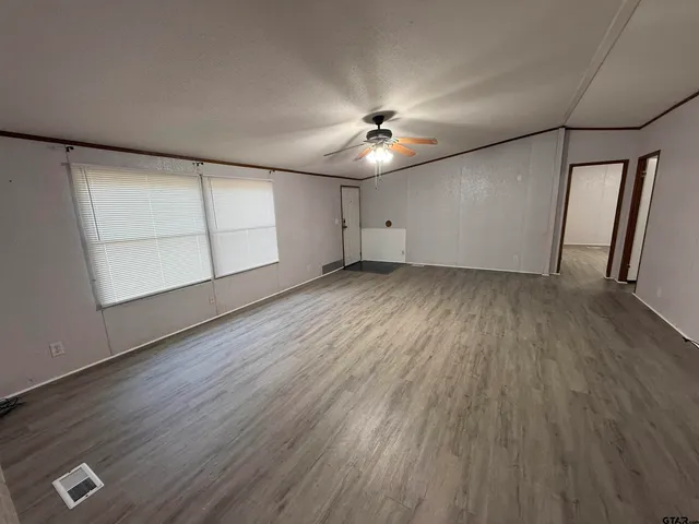 an empty room with wooden floor chandelier fan and windows