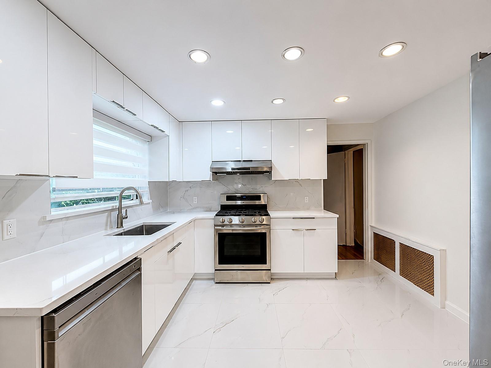 217-41 Stewart Road Queens, NY 11364 - Photo 1 of 11 Kitchen featuring white glossy cabinetry, stainless steel appliances, recessed lighting, and white tile flooring