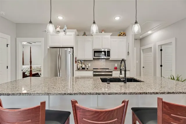 a kitchen with stainless steel appliances kitchen island granite countertop a stove a refrigerator a sink a dining table and chairs with wooden floor