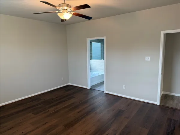 a view of an empty room with wooden floor and a ceiling fan