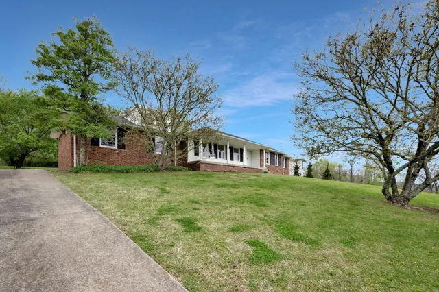 a brick house next to a yard with large trees