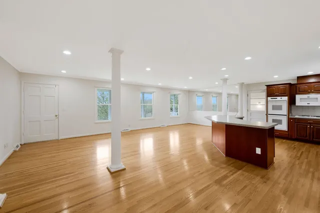 an empty room with wooden floor and kitchen view