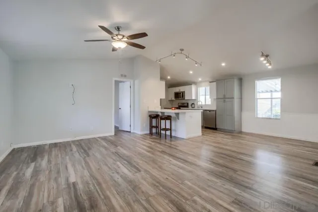 a view of an empty room with kitchen appliances and a ceiling fan