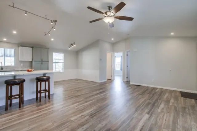 a view of an empty room and kitchen with wooden floor