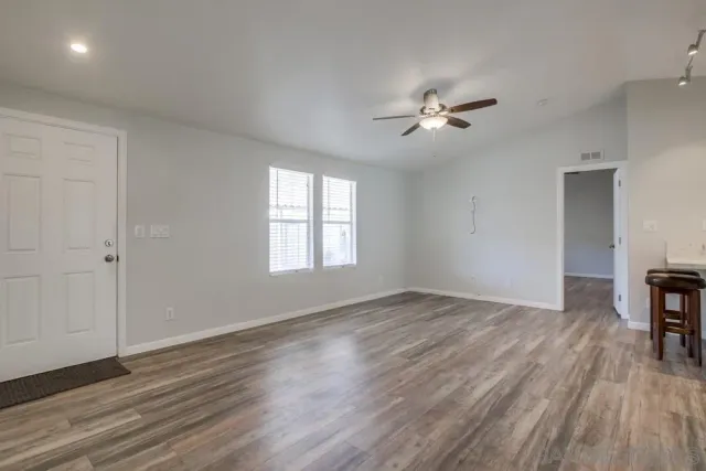 an empty room with wooden floor ceiling fan and windows