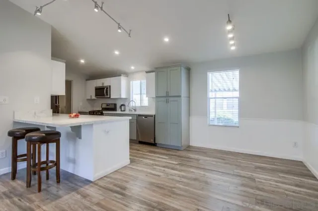 a kitchen with stainless steel appliances granite countertop a stove a sink a refrigerator and white cabinets with wooden floor