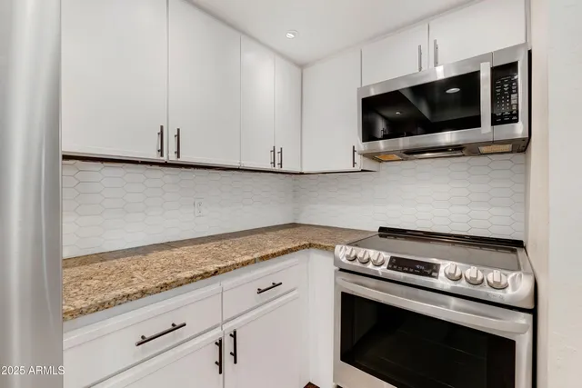 a kitchen with stainless steel appliances granite countertop white cabinets and a stove top oven
