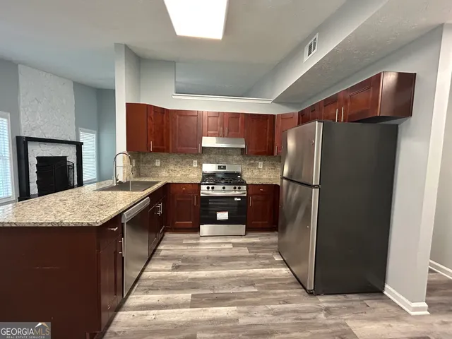 a kitchen with stainless steel appliances granite countertop a refrigerator a stove and a sink with wooden cabinets