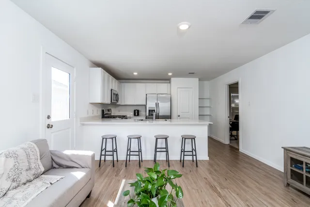a living room with stainless steel appliances furniture wooden floor and a kitchen view
