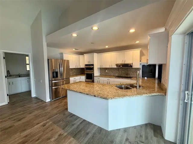 a large kitchen with stainless steel appliances kitchen island a large counter top and wooden floors
