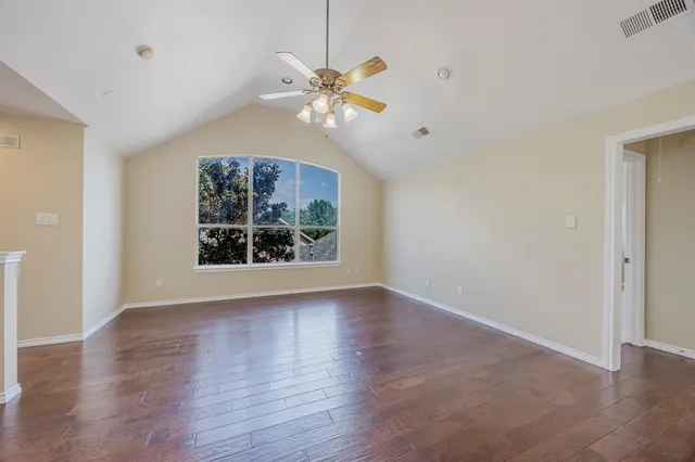 an empty room with wooden floor chandelier fan and windows