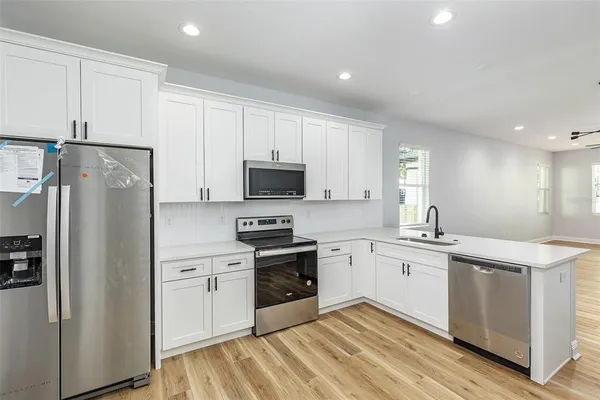 a kitchen with stainless steel appliances granite countertop a stove top oven a refrigerator and white cabinets with wooden floor
