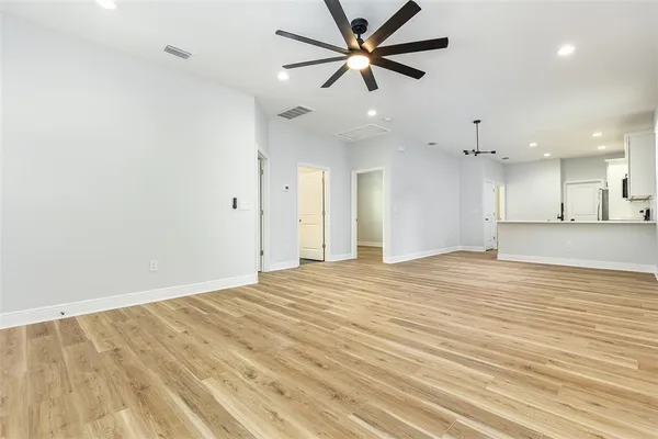 an empty room with kitchen view and a ceiling fan