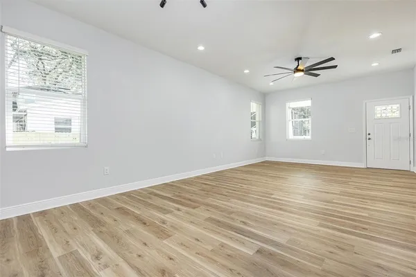 an empty room with wooden floor ceiling fan and windows