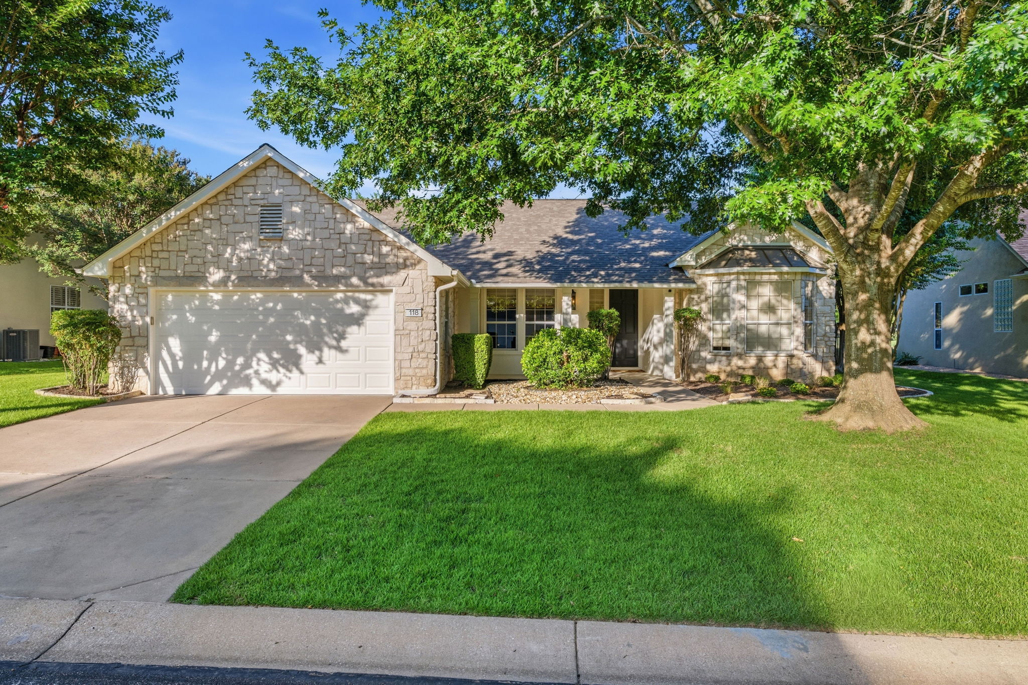 A classic facade with a mix of stone and siding, framed by mature trees and a vibrant green lawn.